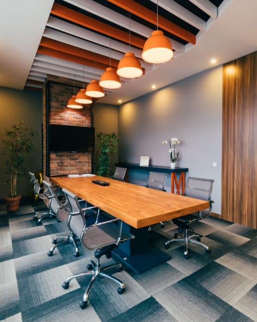 Office setting with a wooden table, orange ceiling lights and metal swivel chairs